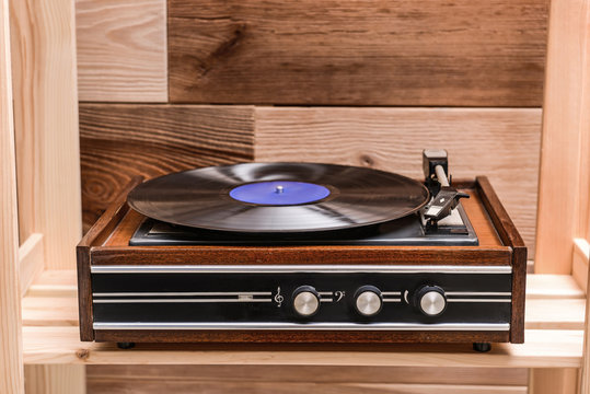 Record player with vinyl disc on wooden shelf