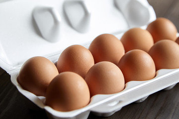 Eggs in tray. Ten chicken eggs in a white container on a brown wooden table