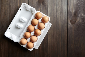 Eggs in tray. Ten chicken eggs in a white box on a brown wooden table with copy space. Top view