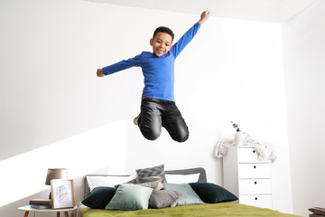 Happy African-American boy jumping on bed at home