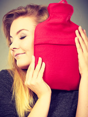 Woman hugs hot water bottle in red fleece cover