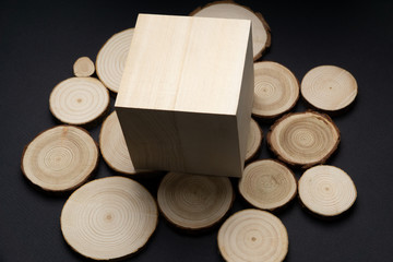 Pine tree cross-sections with annual rings and wooden cube on black surface. Lumber piece close-up shot.