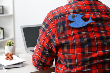 Paper fish on back of young man working in office. April Fool's Day prank