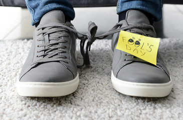 Man with tied together shoelaces and sticky note with text FOOL'S DAY. April Fool's Day prank