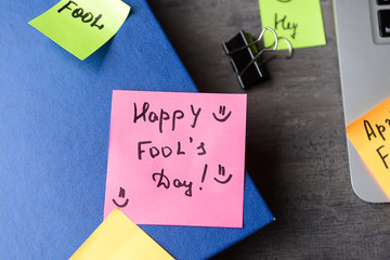Notebook and sticky note with text HAPPY FOOL'S DAY on grey table, closeup