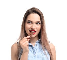 Beautiful young woman eating tasty chocolate on white background