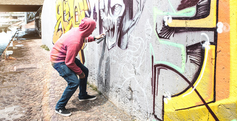 Street artist painting colorful graffiti on public wall - Modern art concept with urban guy performing and preparing live murales with multi color aerosol spray - Bright retro vintage filter