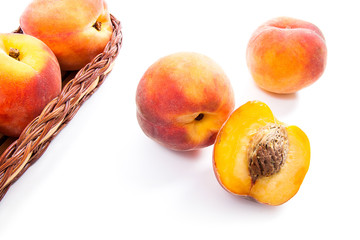 Whole and half of ripe peach fruit and several in basket isolated on white background.
