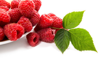 Small plate with ripe raspberries and green leaf isolated on white background.
