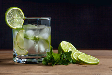 Summer cocktail mojito in glass, sliced lime and mint on wooden background..