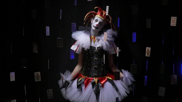 Amazing female jester is surrounded by cards in the dark