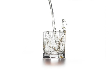 Whiskey pouring into glass with ice on light background..