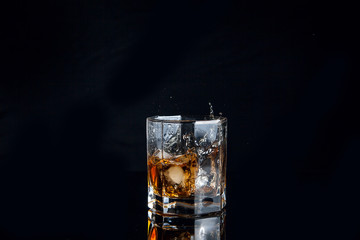 Whiskey splash from the fallen ice cube into glass with beverage isolated on black background..