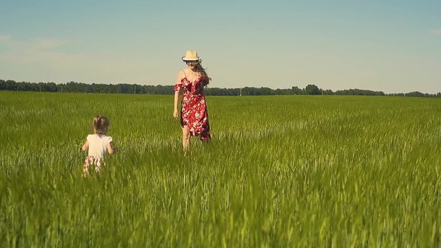Slow motion: Young mother plays with child in the field, dressed in red dress that flutters in the wind. She whirls in arms, smiles.