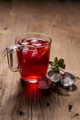 Hibiscus cold tea with ice and mint on vintage wooden background.