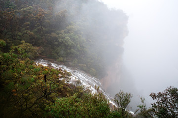 Fototapeta na wymiar Waterfall flows off the cliff into the foggy abyss