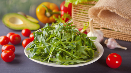 Wet fresh arugula on the plate with vegetables on the background. Cool-season herbs. Plant, used in cooking.