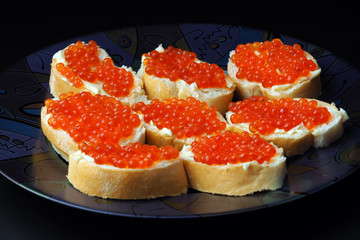 Red caviar on sandwiches and lemon on a black background