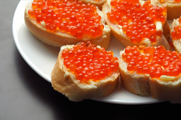 Naklejka na ściany i meble Red caviar on sandwiches in a plate on a dark background