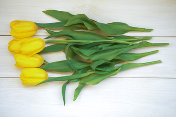 Yellow tulips lie on a white wooden table.