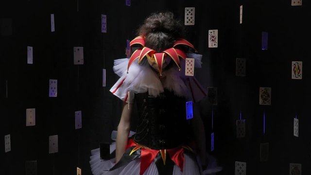 Joker woman with makeup and a colorful dress is standing in the dark like a puppet then drops her head and arms, slow motion