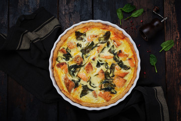 Homemade quiche tart with red fish and spinach on dark wooden background. Vintage style. Top view.