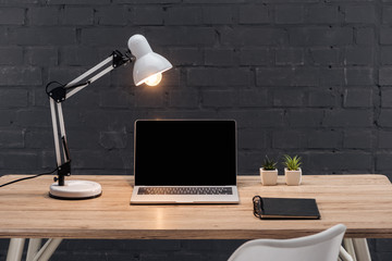 modern workplace with laptop with blank screen, plants, bright lamp and notebook on wooden table...
