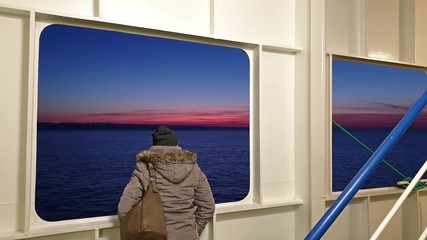 Lady looking through the scuttle while Irish ferry is leaving Cherbourgh in France to Dublin harbour during sunset - Ireland
