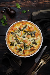 Homemade quiche tart with red fish and spinach on dark wooden background. Vintage style. Top view.
