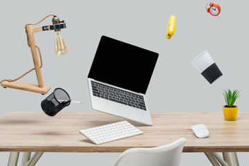 laptop with blank screen and stationery levitating in air at workplace isolated on grey