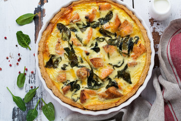 Homemade quiche tart with red fish and spinach on light wooden background. Vintage style. Top view.