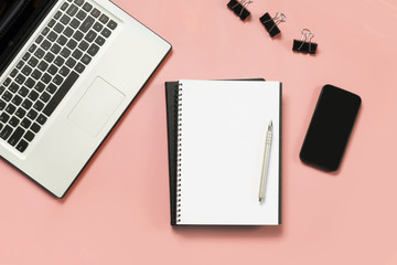 Workplace with open laptop, white and black accessory on pink. Top view and copy space.