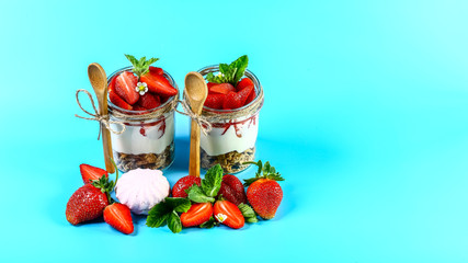 Strawberry cheesecake in glass jar with fresh strawberries and cream cheese Isolated on a blue background. Copy space. Healthy homemade dessert