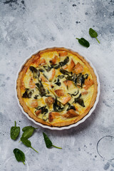 Homemade quiche tart with red fish and spinach on light wooden background. Vintage style. Top view.