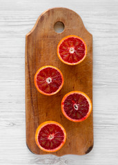 Blood oranges halved on rustic wooden board over white wooden background, top view. Flat lay,...