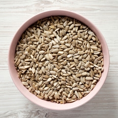 Raw hulled sunflower seeds in a pink bowl over white wooden background. Flat lay, top view, from above. Close-up.