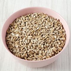 Dry hulled sunflower seeds in a pink bowl over white wooden background, low angle view. Closeup.