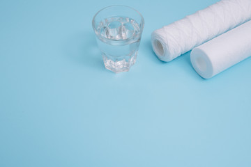 Water filters. Carbon cartridges and a glass on a blue background. Household filtration system.