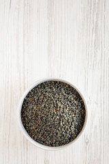 Top view, organic green french lentils in gray bowl over white wooden surface, top view. Flat lay, overhead, from above. Copy space.