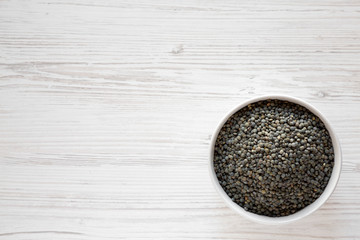Organic green french lentils in gray bowl over white wooden surface, top view. Flat lay, overhead, from above. Copy space.