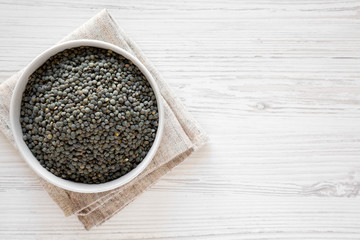 Top view, dry green french lentils in gray bowl over white wooden background. Flat lay, top view, from above. Copy space.