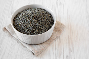 Dry green french lentils in gray bowl over white wooden background, low angle view. Close-up.