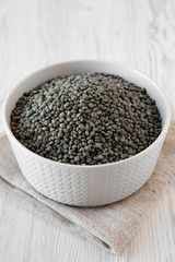 Green french lentils in gray bowl over white wooden background, low angle view. Close-up.