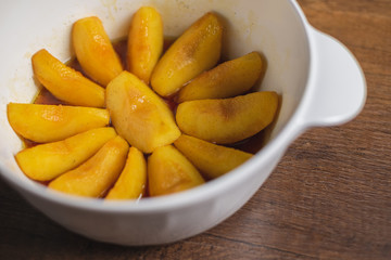 Cooked apple pieces with caramel arrange in a white bowl on wood table top.