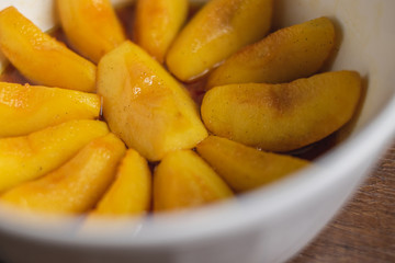 Cooked apple pieces with caramel arrange in a white bowl on wood table top.
