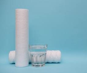Water filters. Carbon cartridges and a glass on a blue background. Household filtration system.