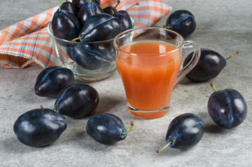 Plum juice in a mug and ripe plums on a gray table.