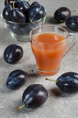 Plum juice in a mug and blue plums on a gray table.