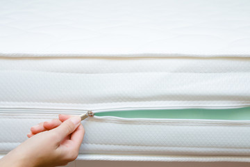 Woman's hand opening cover of new mattress with zipper. Checking hardness and softness. Choice of...