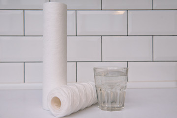 Water filters. Carbon cartridges and a glass on a white background. Household filtration system.